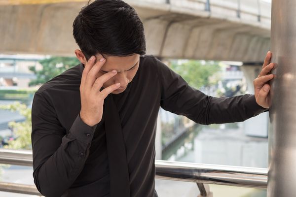 man with headache outside leaning against a wall 