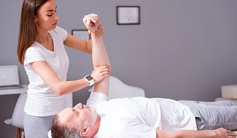 physiotherapist works on older male patients arm