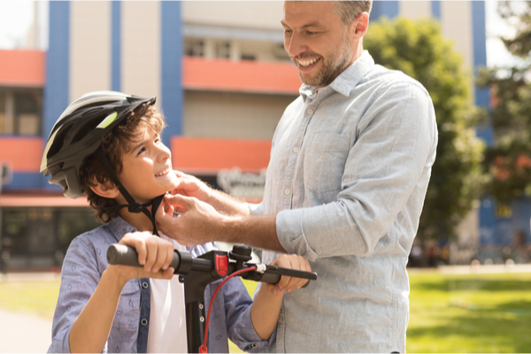 A man helping a child put on a helmet outdoors