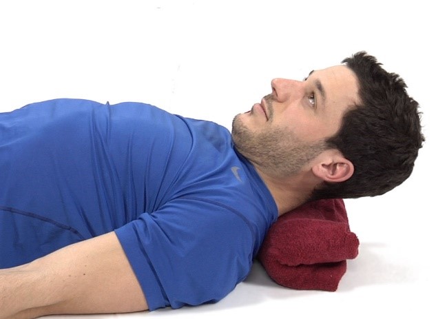 a man lying down with a rolled up towel underneath his head